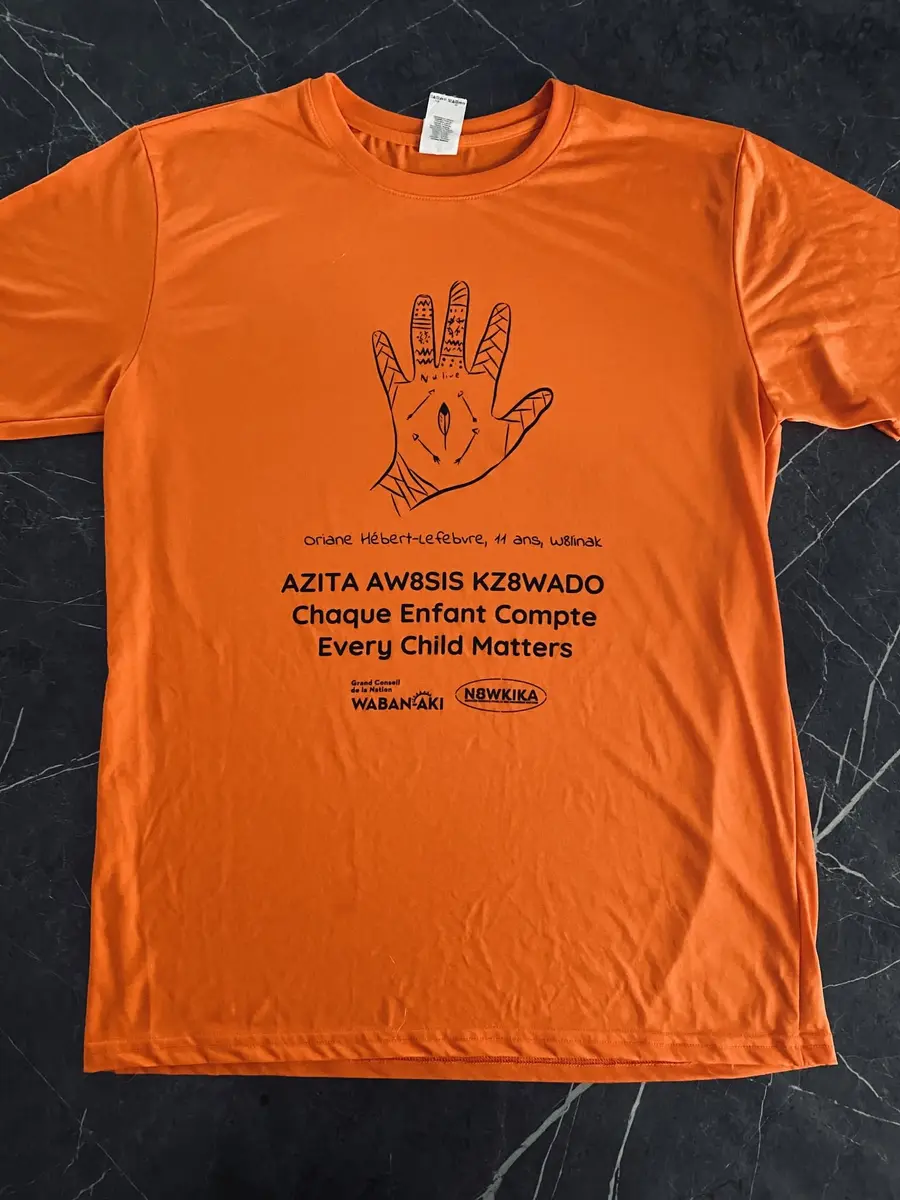 Chandail orange W8banaki « Chaque enfant compte » — dessin d'une enfant de Wôlinak, message en abénaquis AZITA AW8SIS KZ8WADO